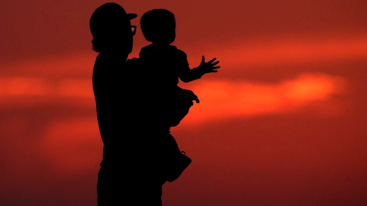 FILE - In this June 26, 2020 file photo, a man and his son are silhouetted against the sky as they watch the sunset from a park in Kansas City, Mo. Health experts once thought 2020 might be the worst year yet for a rare paralyzing disease that has been hitting U.S. children for the past decade. But they now say the coronavirus pandemic could disrupt the pattern for the mysterious illnesses, which spike every other year starting in late summer.