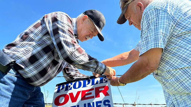 Gaylen Dewing, left, and Marvin Abraham affix a sign to a roadside fence east of Bismarck,...