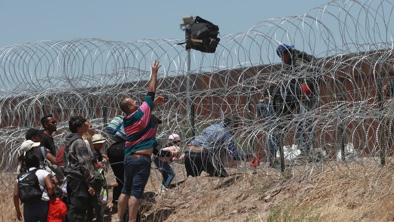 FILE - Migrants cross a barbed-wire barrier at the US-Mexico border, as seen from Ciudad...